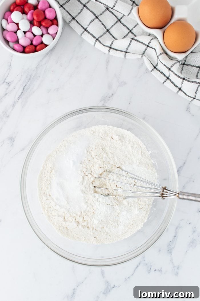 A glass bowl containing the pre-mixed dry ingredients—flour, baking soda, cornstarch, and salt—with a whisk ready to ensure even distribution.