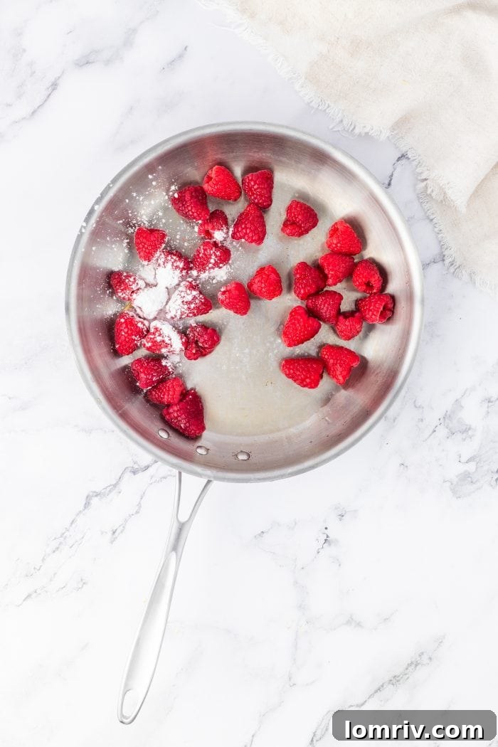 A saucepan on the stove with fresh raspberries and cornstarch, beginning to cook down.