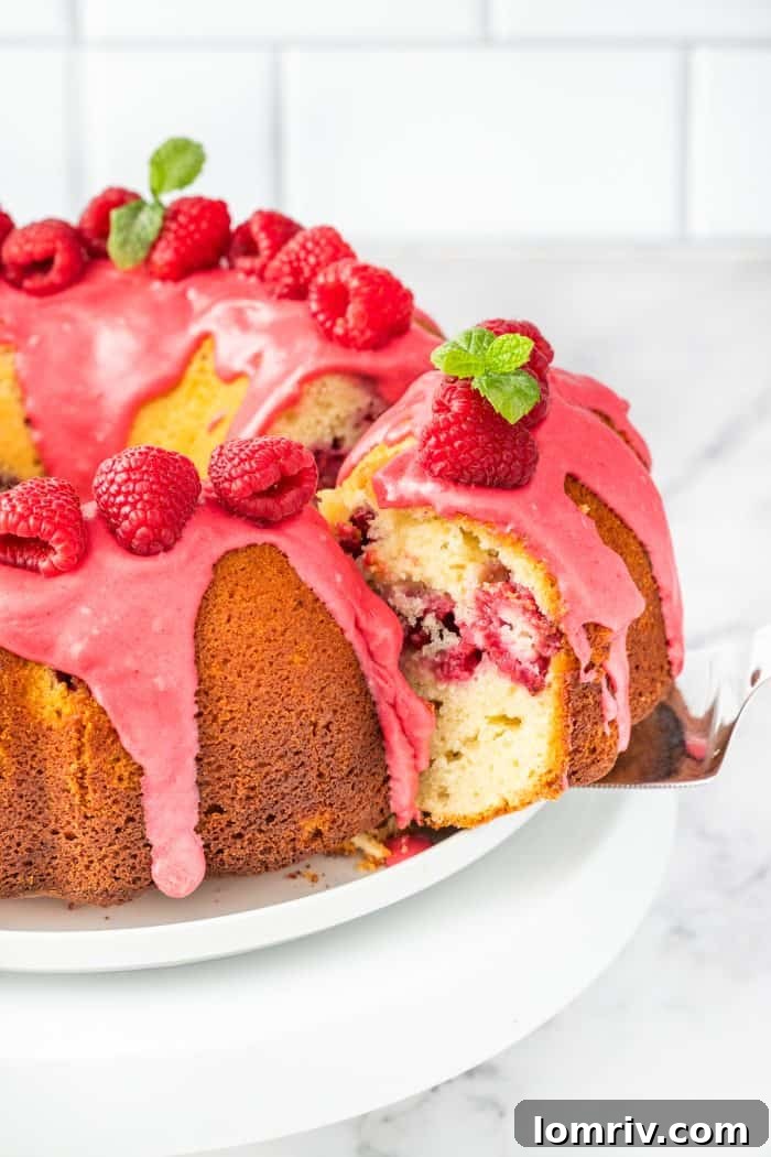 A lemon raspberry bundt cake with a slice being removed, revealing the moist interior and raspberry pieces.