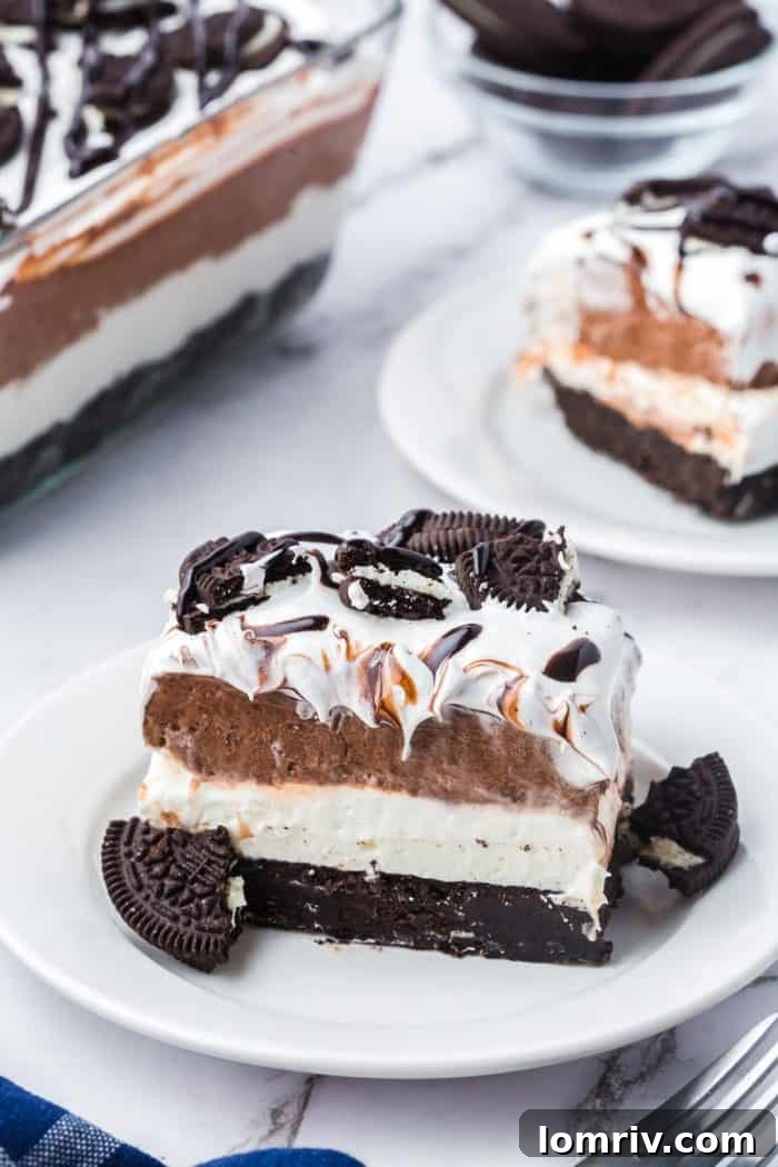 Two plates with slices of no bake Oreo layered dessert with the glass dish with the dessert in it in the background.
