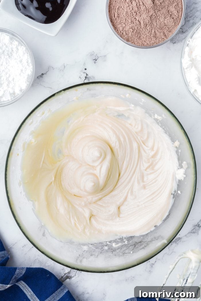 A glass mixing bowl with cream cheese that has been mixed with a stand mixer.