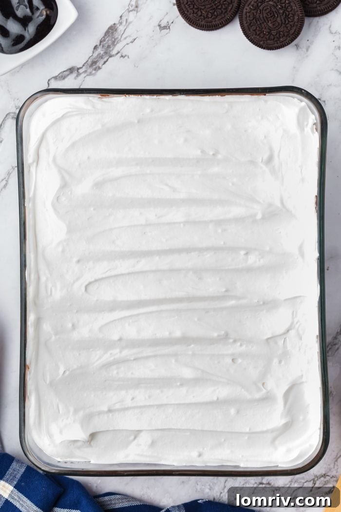 Cool Whip spread over the chocolate pudding layer in a glass dish.