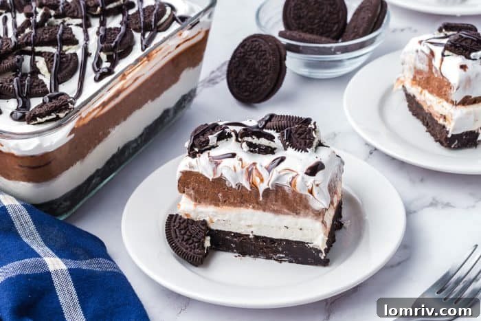Two plates with slices of no bake Oreo layered dessert and the glass dish with the rest of the dessert.