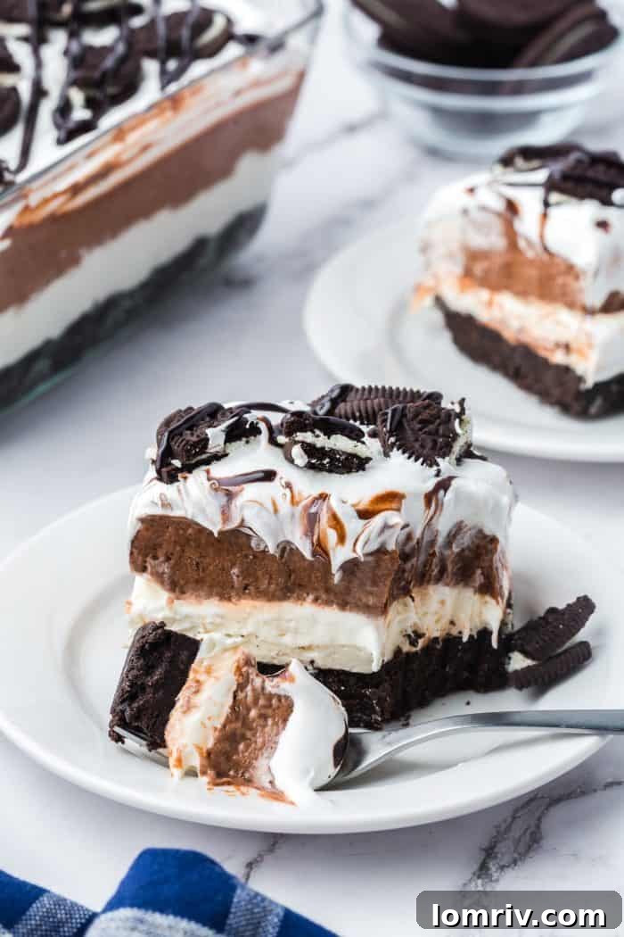A plate with a slice of no bake Oreo dessert with a bite taken out of it.