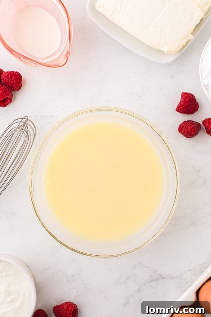 A smooth, melted white chocolate ganache mixture in a glass bowl, ready to be incorporated into the cheesecake batter.