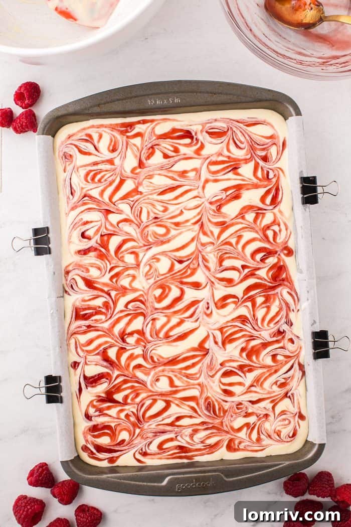 The unbaked white chocolate raspberry cheesecake bars showing the beautiful swirl of raspberry sauce on top of the creamy filling.