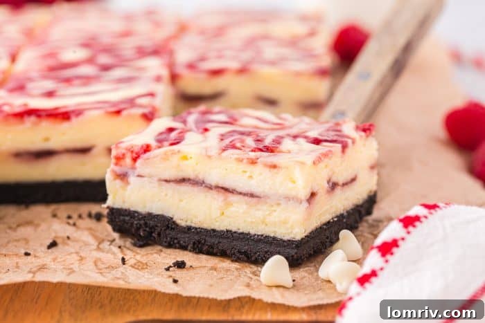 A close-up view of a single white chocolate raspberry cheesecake bar resting on parchment paper, adorned with white chocolate chips.