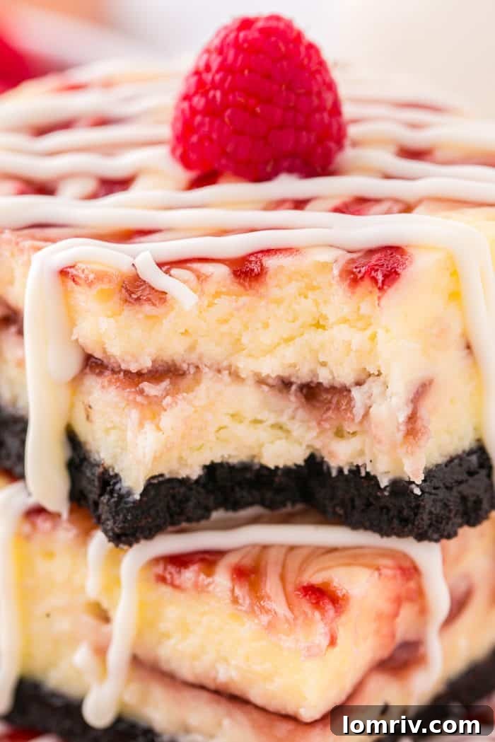 An inviting, up-close image of two white chocolate raspberry cheesecake bars, one with a delightful bite taken out of it.