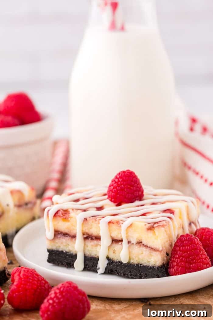 A single white chocolate raspberry cheesecake bar on a white plate, garnished with fresh raspberries, with a bottle of milk in the soft-focused background.