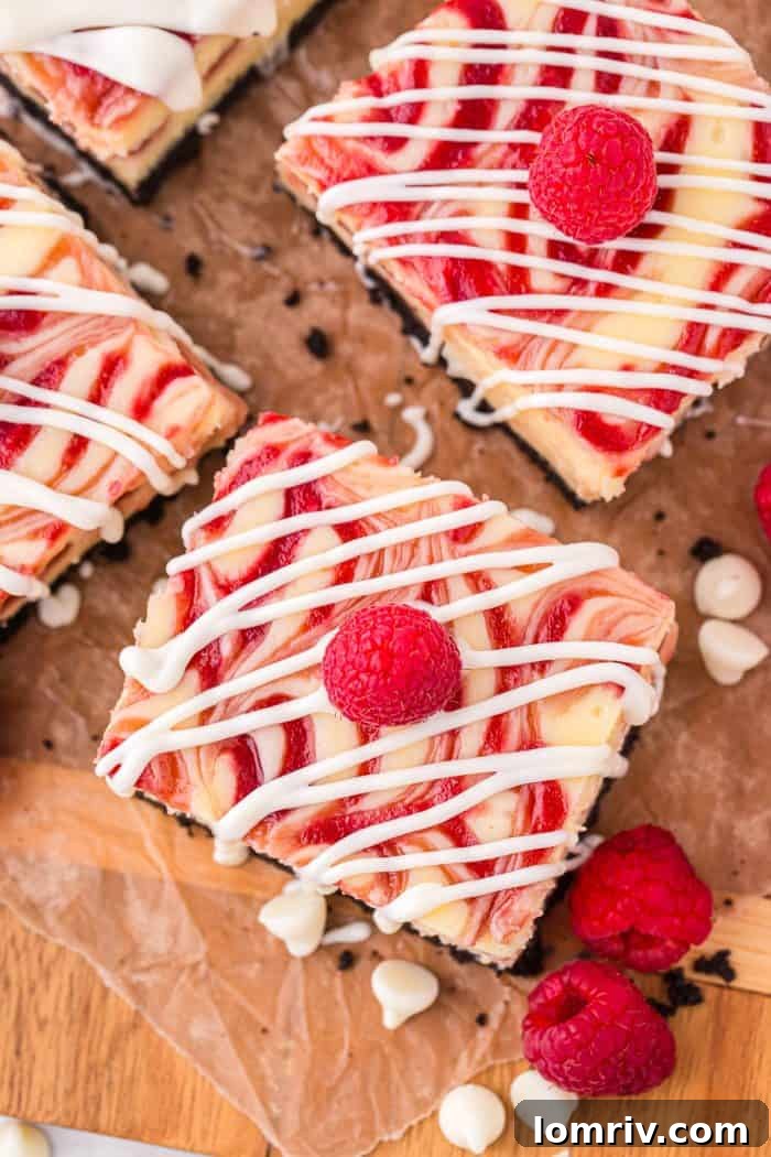 An inviting overview of three white chocolate raspberry cheesecake bars artfully drizzled with white chocolate, resting on parchment paper with fresh raspberries scattered around.