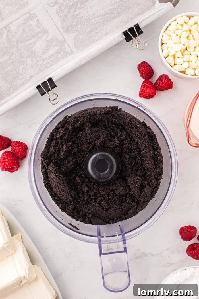A food processor bowl filled with finely crushed Oreo cookie crumbs, ready for the next step of making the cheesecake crust.