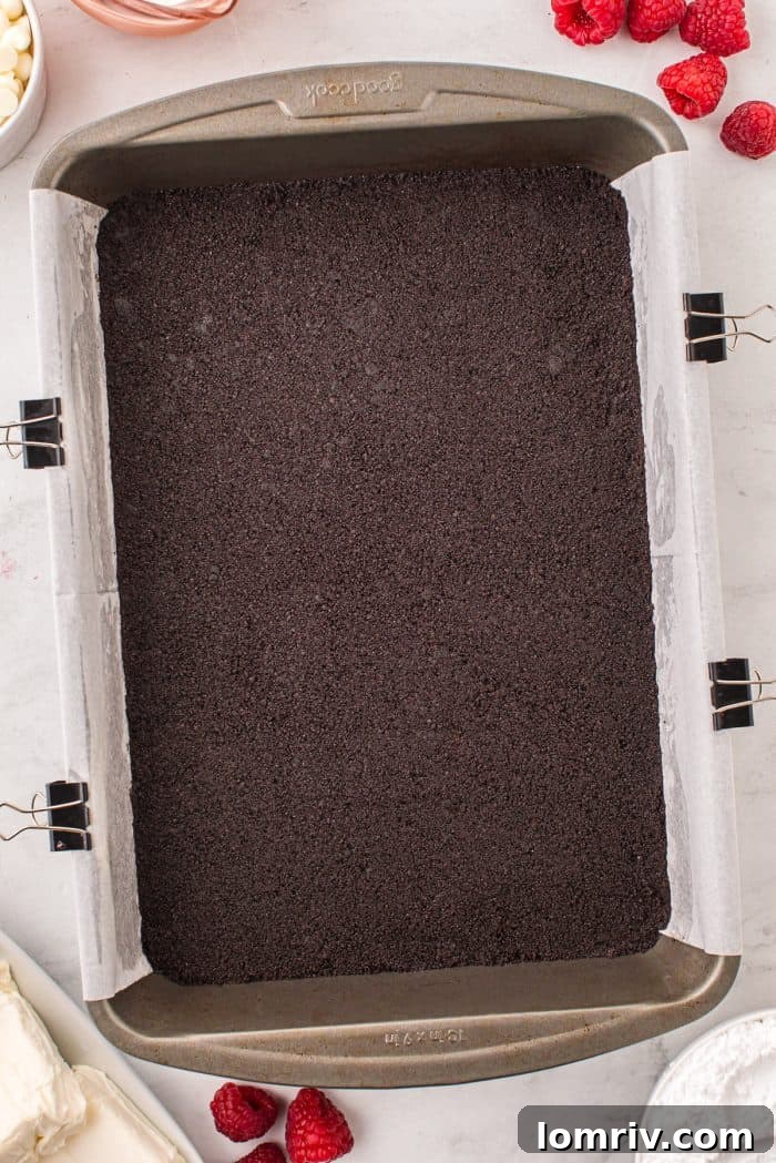 The perfectly pressed Oreo cookie crumb crust covering the bottom of a baking pan, ready for the cheesecake filling.