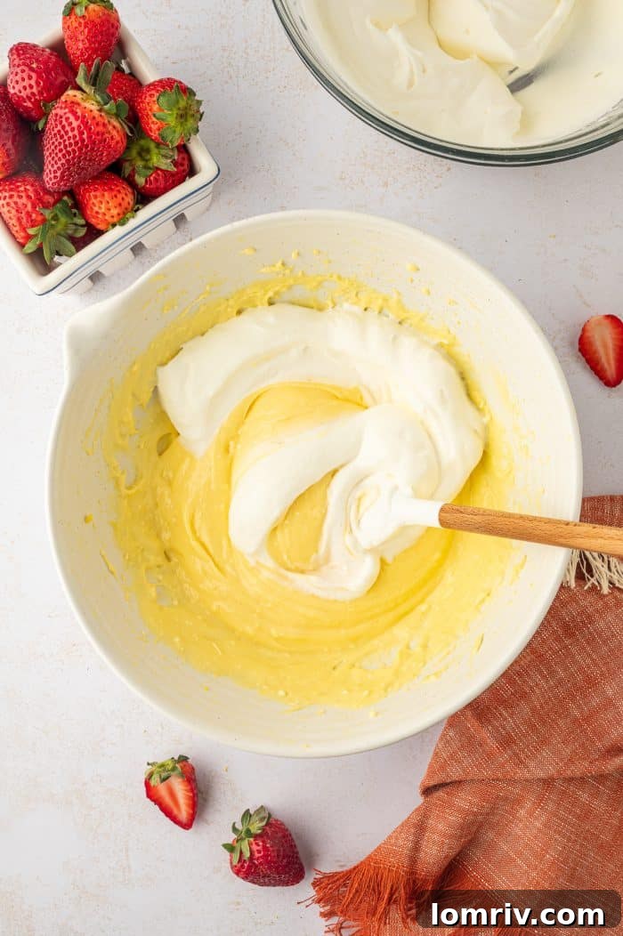 A spatula gently folding freshly whipped cream into the vanilla pudding mixture in a glass bowl.