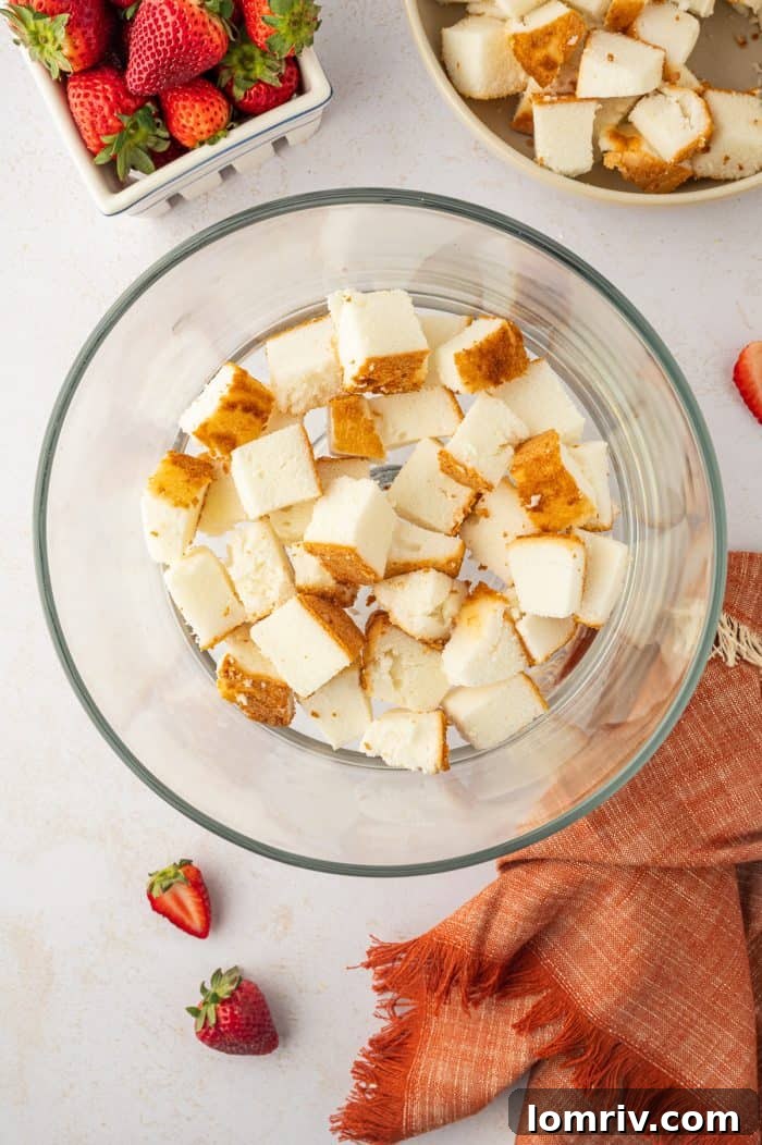 The initial layer of cubed angel food cake neatly arranged at the bottom of a clear trifle bowl, forming the base.