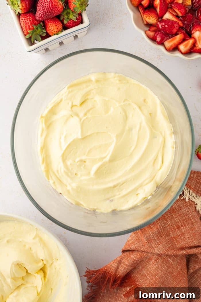 A smooth, creamy layer of vanilla pudding mixture spread evenly over the strawberries in the trifle bowl, completing one cycle of layers.
