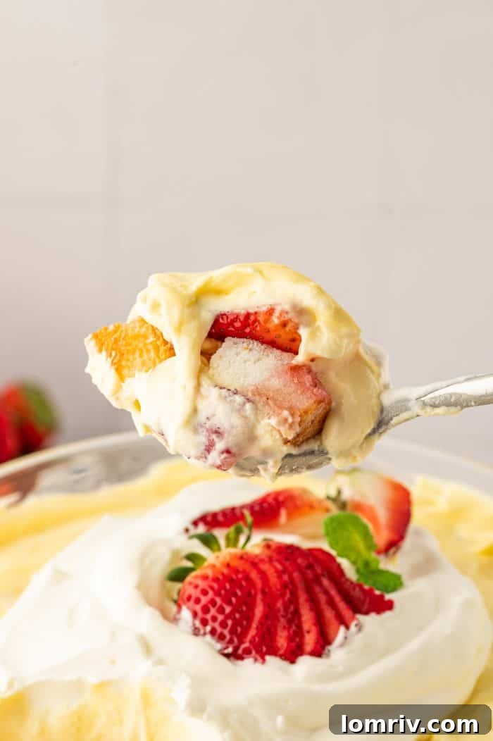 A perfect scoop of strawberry trifle lifted from the main bowl, showcasing its defined layers, with the whole trifle in the background.