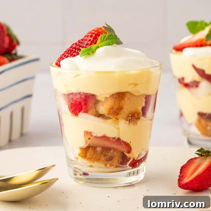Two glass filled with strawberry trifle with strawberries in the background and gold spoons.