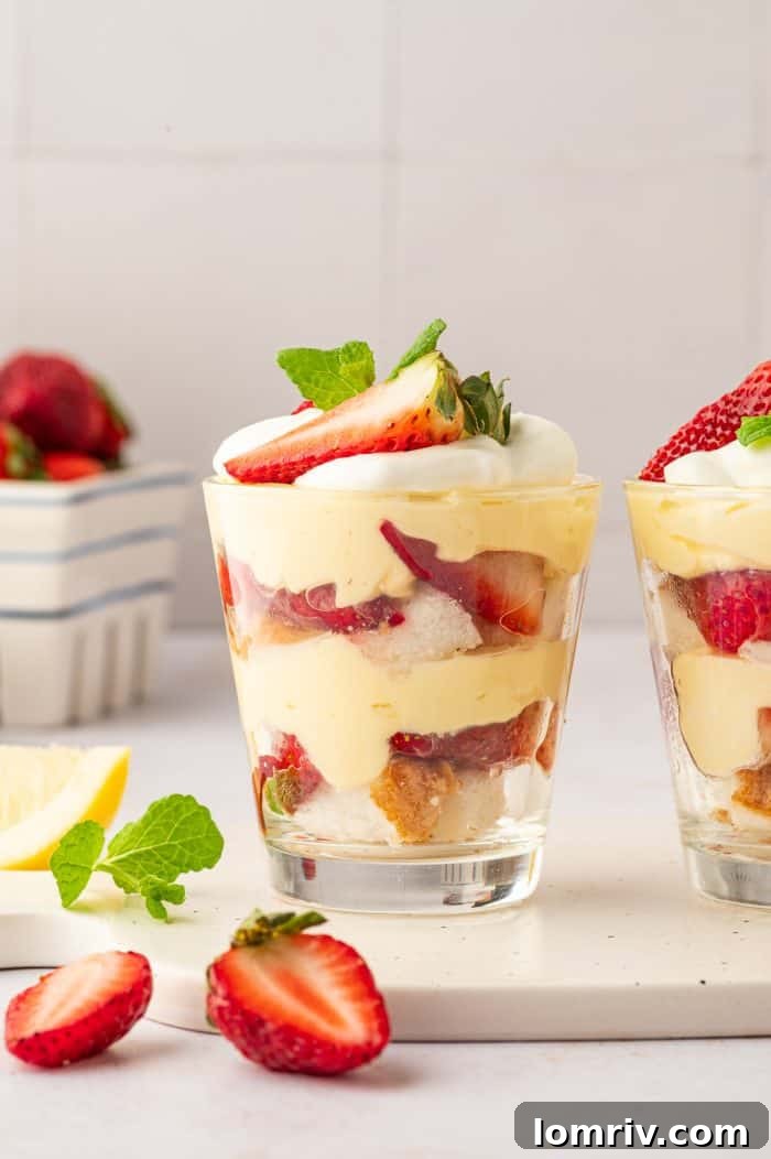 Two small glass desserts filled with layered strawberry trifle, fresh strawberries visible in the background creating a vibrant scene.