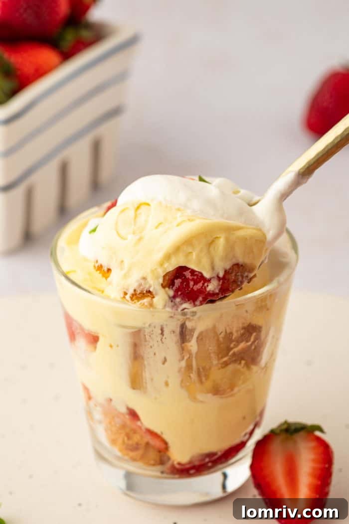 A spoon scooping a perfect bite of strawberry trifle from a glass, highlighting the distinct layers and the fresh fruit.