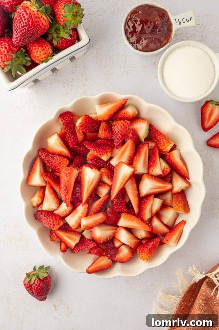 A pristine white bowl filled with freshly sliced and washed strawberries, glistening and ready for the next step.