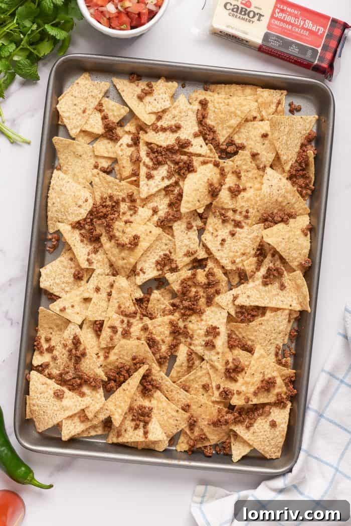 Ground beef added to tortilla chips on a baking pan.