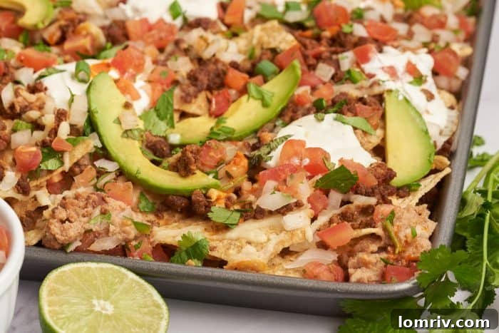 An upclose image of sheet pan nachos showing the sliced avocados and tortilla chips with melted cheese.