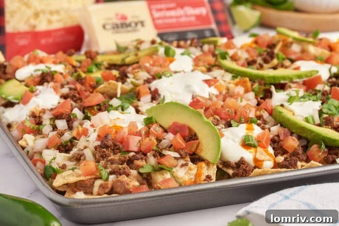 An upclose image of sheet pan nachos showing the sliced avocados and tortilla chips with melted cheese.