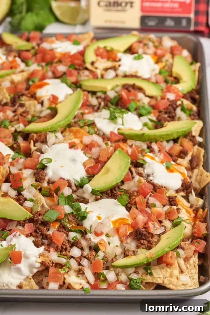 An upclose image of sheet pan nachos showing the sliced avocados and tortilla chips with melted cheese.