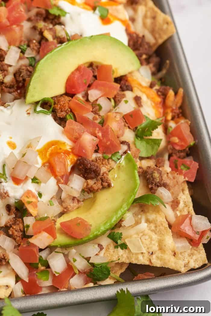 Baked sheet pan nachos with pico de gallo and sliced avocado.