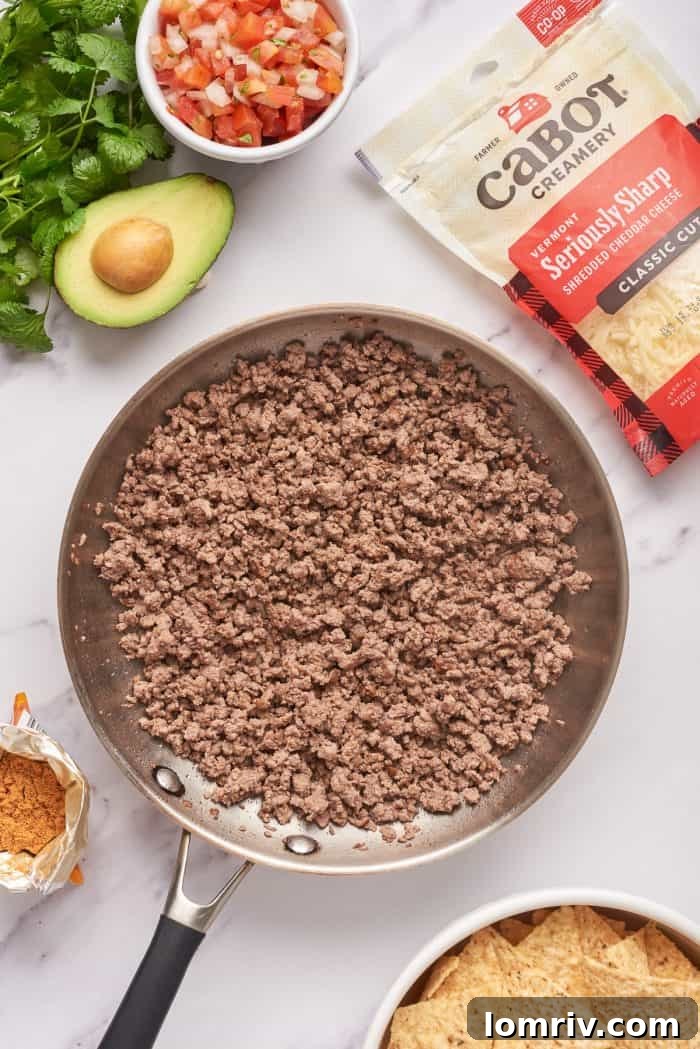 Ground beef cooking in a skillet with half of an avocado beside it.