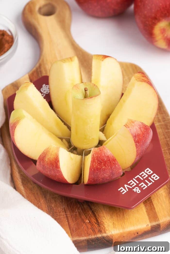 A wooden cutting board with an Envy Apples, apple slicer, slicing through an apple.