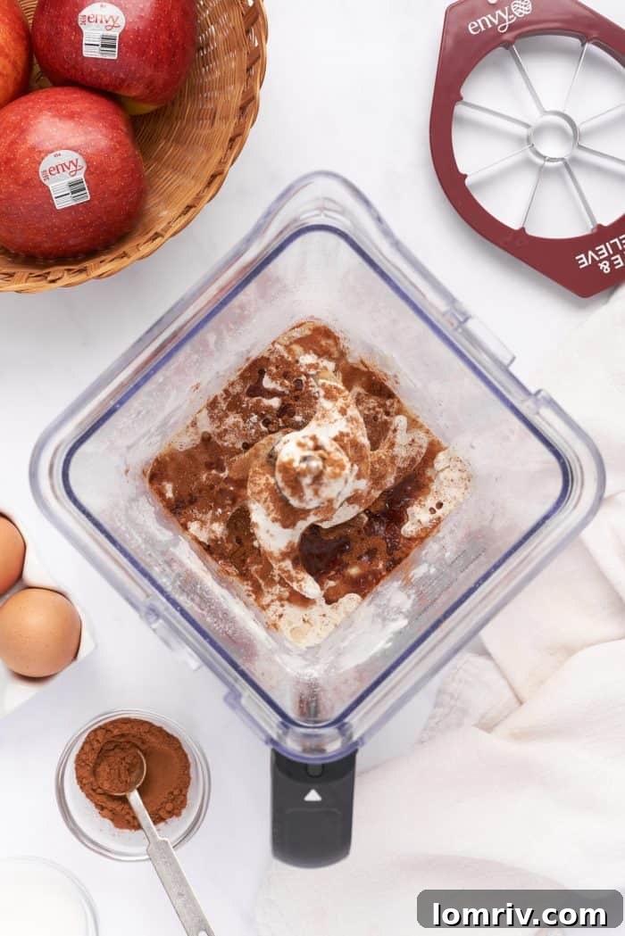 The crepe batter in a blender with apples and cinnamon in the background.