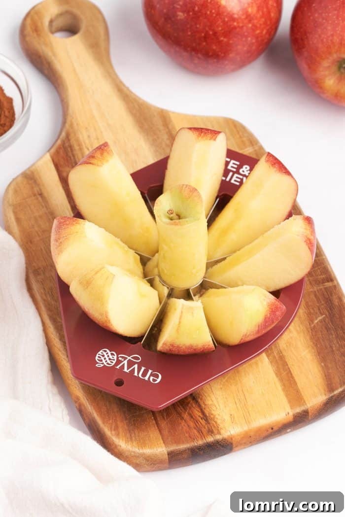 A wooden cutting board with an Envy Apples, apple slicer, slicing through an apple.