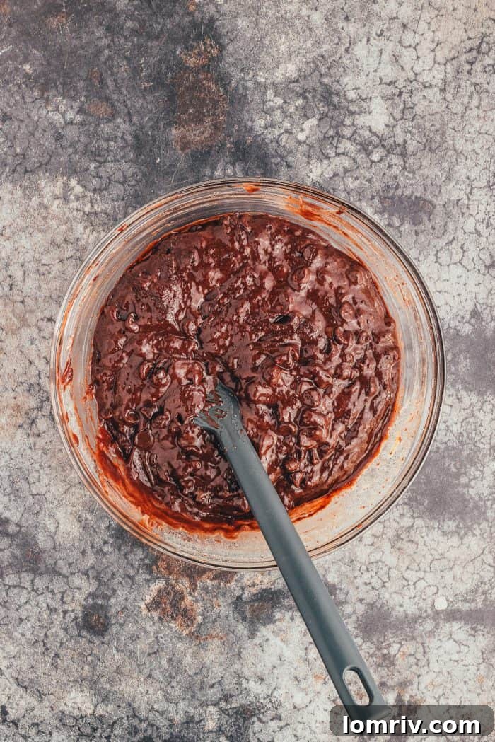A glass bowl with the batter for double chocolate muffins and a spoon. 