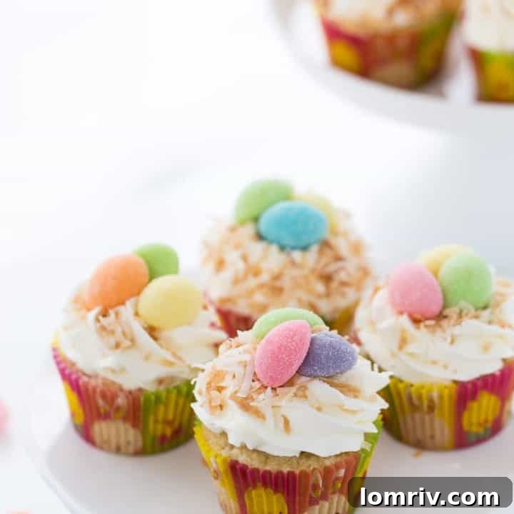 Charming coconut bird nest cupcakes, topped with sweet coconut whipped frosting and toasted coconut flakes, holding candy eggs.