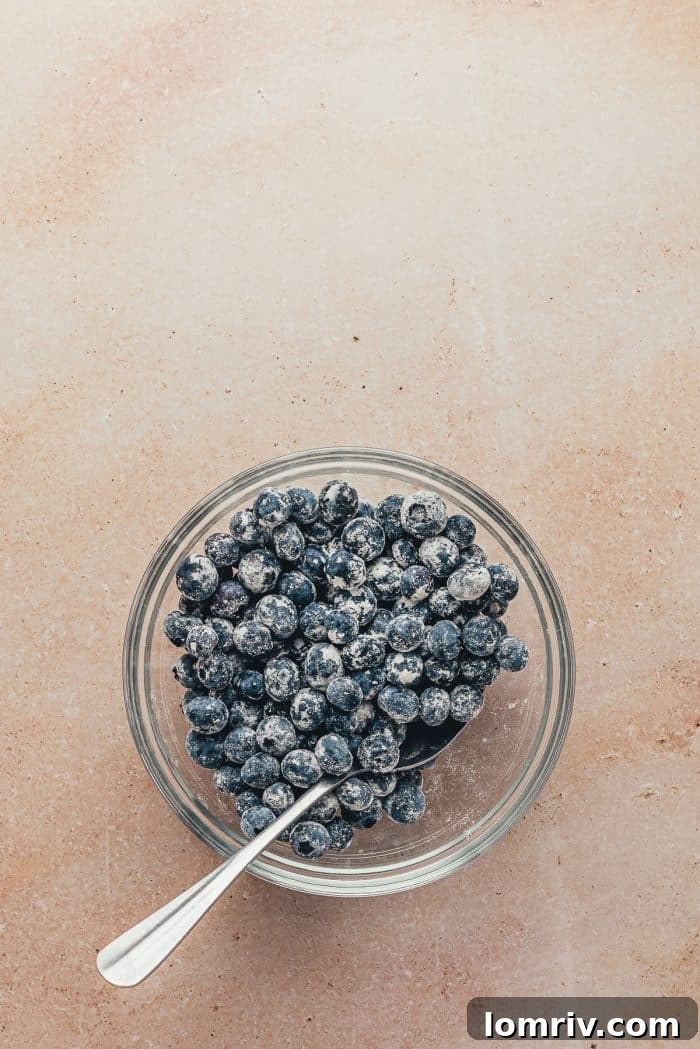 A bowl filled with fresh blueberries, lightly coated in flour, with a spoon resting inside, ready to be incorporated into the cake batter.