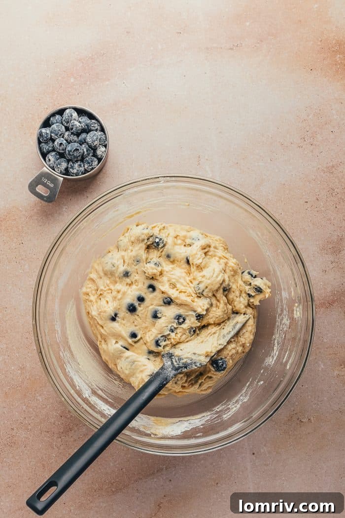 A glass bowl filled with rich cake batter, now beautifully mixed with sweet blueberries, promising a burst of flavor in every bite.