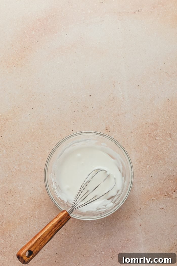 A glass bowl containing a smooth, white icing, with a whisk resting inside, ready for glazing the coffee cake.