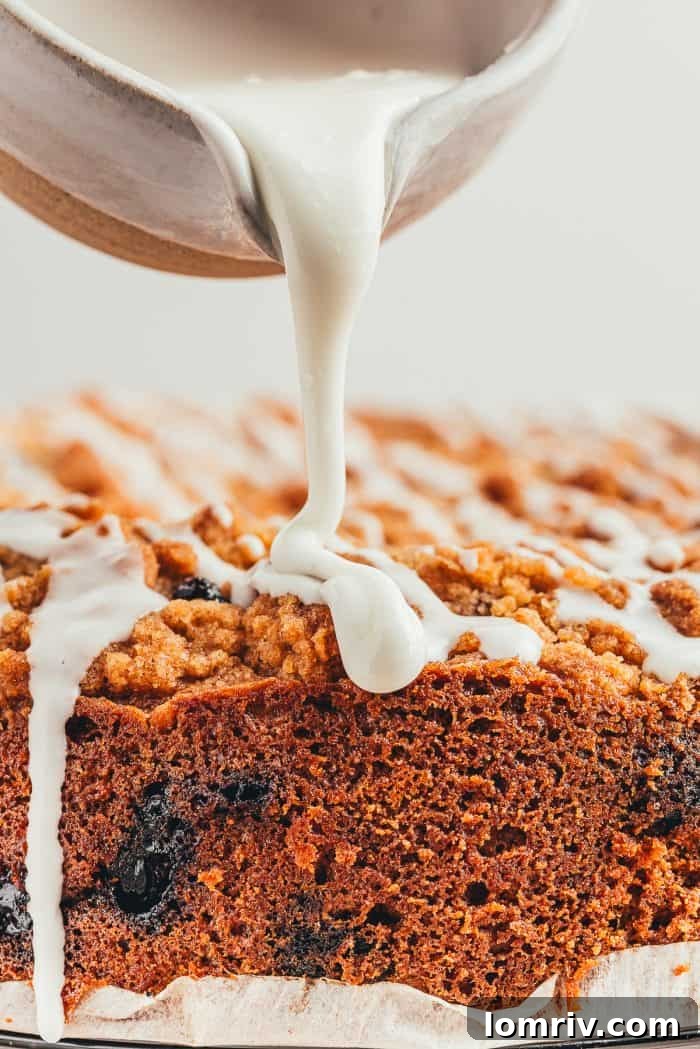 Sweet vanilla icing being gracefully poured over a freshly baked blueberry coffee cake, creating a beautiful finishing touch.