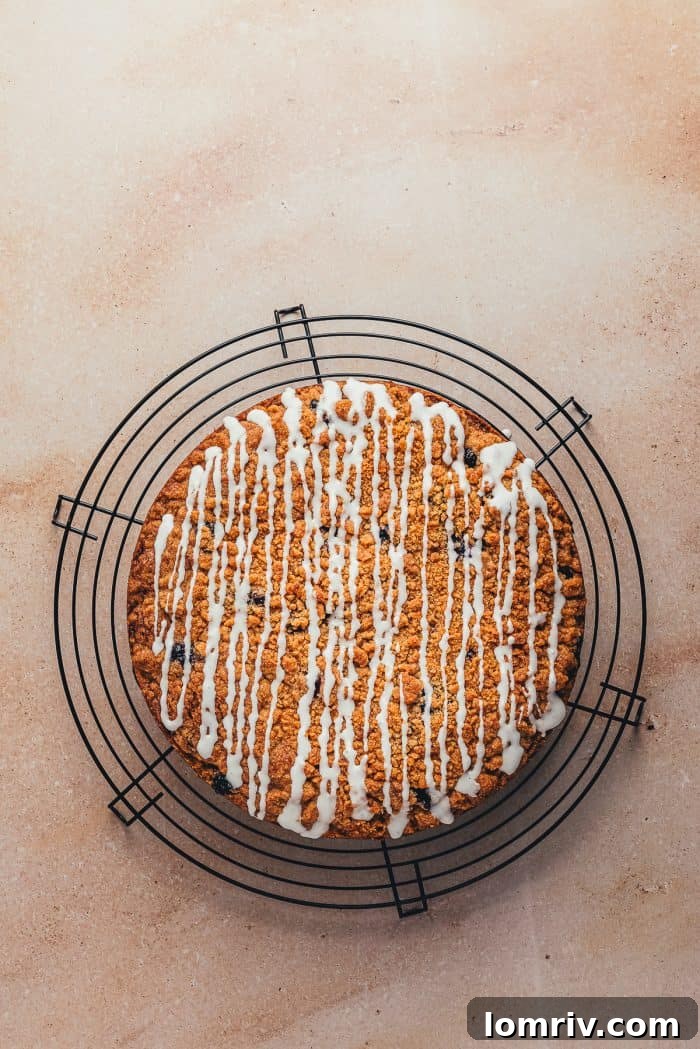 A beautifully glazed blueberry sour cream coffee cake, resting on a cooling rack, with the white icing artfully drizzled across its golden-brown surface.