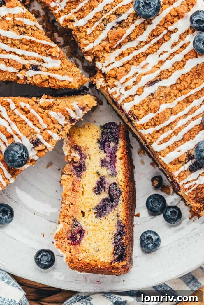 A beautifully baked blueberry coffee cake with several slices already cut, one turned on its side to reveal the moist, blueberry-filled interior.