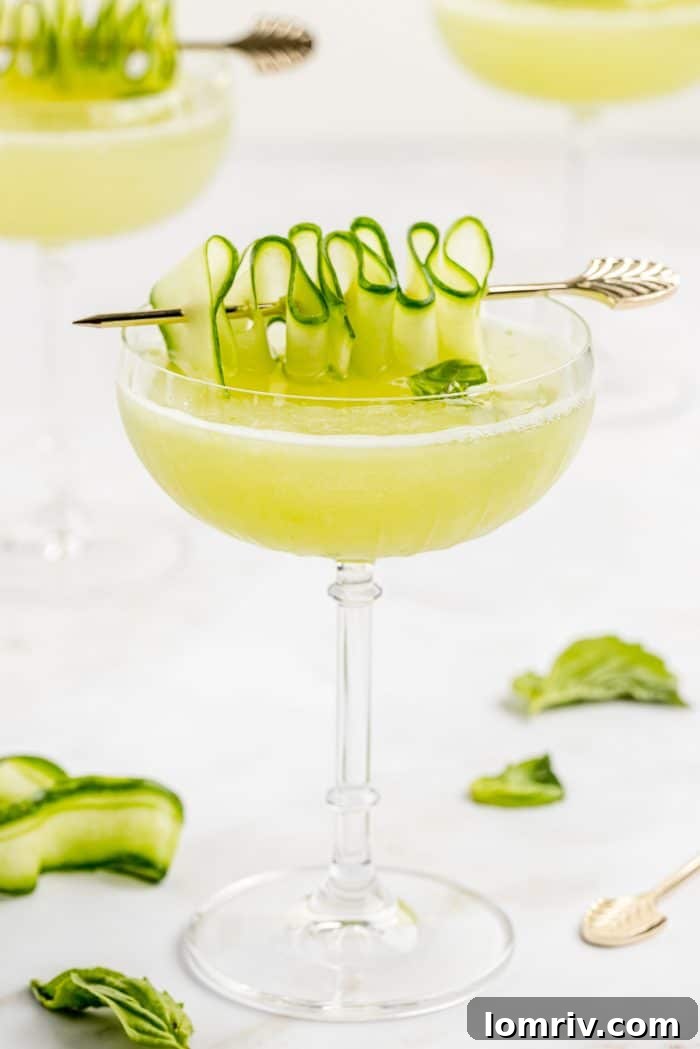 A meticulously prepared Cucumber Basil Gimlet, beautifully garnished with a delicate cucumber ribbon and a fresh basil sprig, ready to be enjoyed.