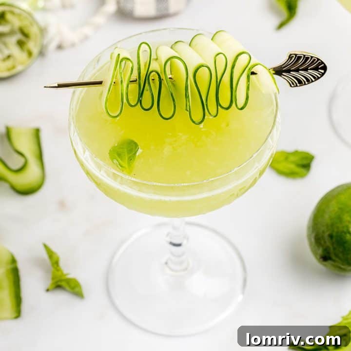 A Cucumber Basil Gimlet with a ribboned cucumber garnish and two other drinks in the background, signaling a delightful gathering.