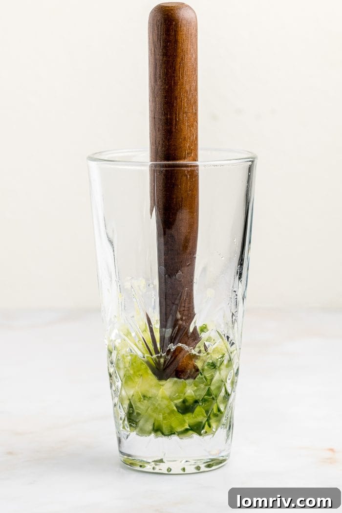 A muddle stick actively crushing fresh cucumber and basil in a cocktail shaker, releasing their vibrant juices and aromas.