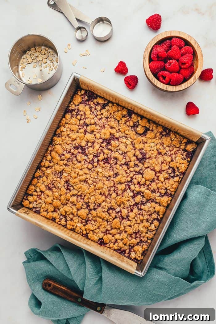The baked raspberry crumble bars with a teal colored towel and fresh raspberries scattered.