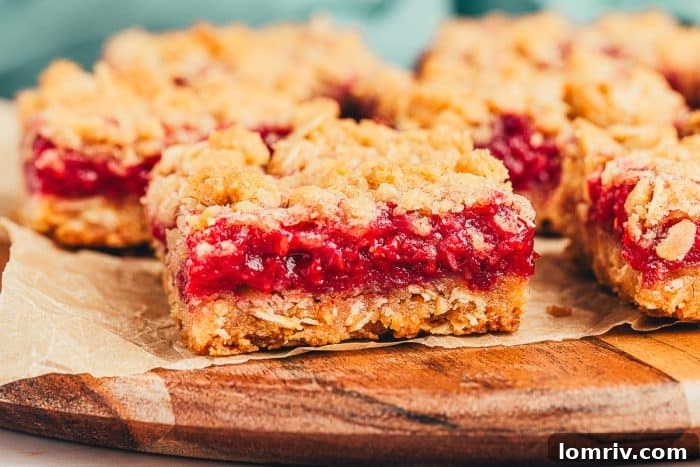 A couple of raspberry crumble bars on parchment paper on a wooden board.