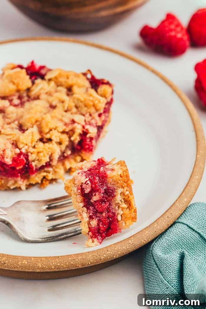 A white plate with a raspberry crumble bar with a fork taking a bite out of the bar.