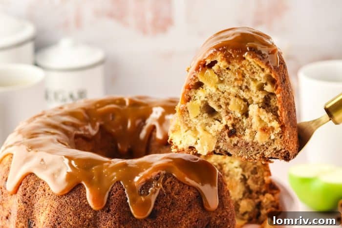 A perfect slice of Caramel Apple Bundt Cake is gracefully lifted from the cake, emphasizing its fluffy texture, apple chunks, and creamy swirl.