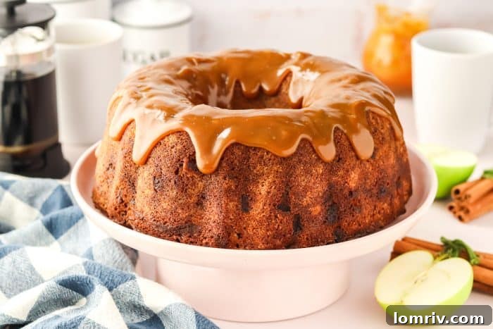 The whole, spectacular Caramel Apple Bundt Cake, beautifully glazed with caramel, stands proudly on a white cake stand, a centerpiece for any fall celebration.