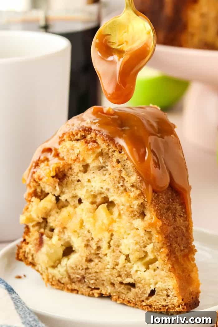 A close-up shot of a single slice of moist apple Bundt cake, being luxuriously drenched with a stream of golden caramel sauce, highlighting the dessert's irresistible appeal.